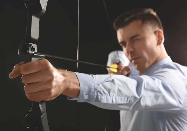 Joven hombre de negocios practicando tiro con arco sobre fondo oscuro — Foto de Stock