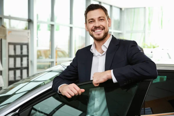 Красивый продавец автомобилей стоит рядом с автомобилем в дилерском центре — стоковое фото