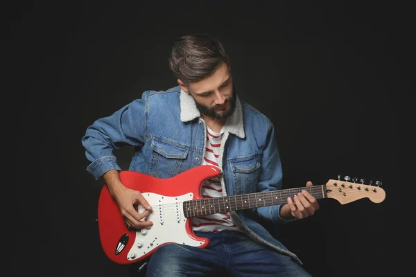 Joven músico guapo tocando la guitarra sobre fondo negro — Foto de Stock