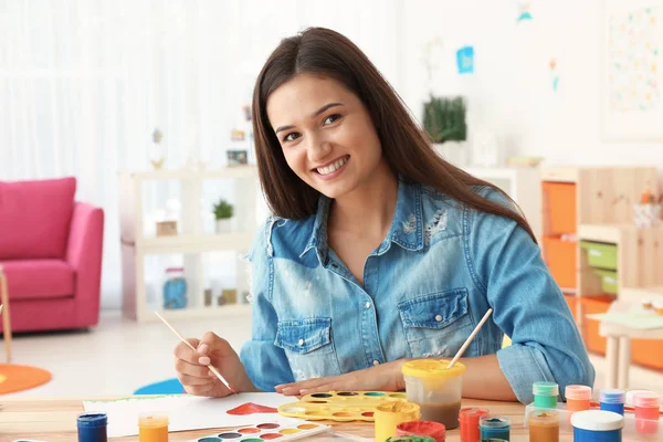 Mooie jonge vrouw schilderij hart aan tafel in de kamer — Stockfoto