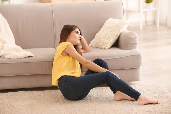 Молода жінка сидить на килимі біля дивана вдома — стокове фото