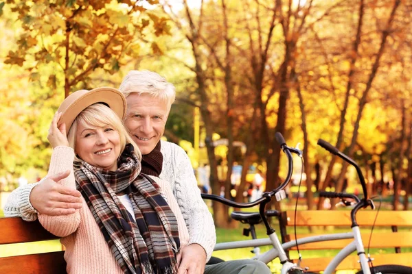 Cute elderly couple sitting on bench in autumn park — Stock Photo, Image