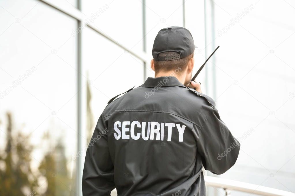 Male security guard using portable radio transmitter near building outdoors