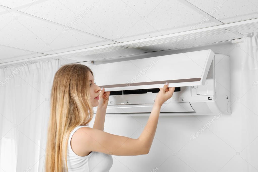 Young woman checking air conditioner at home