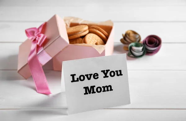 Nota com palavras "Amo você mãe" e caixa de deliciosos biscoitos no fundo claro — Fotografia de Stock