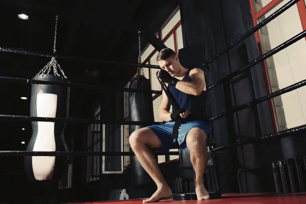 Boxer masculino aplicando envoltórios de mão enquanto se prepara para o treinamento em ginásio — Fotografia de Stock