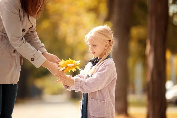 Mutter gibt ihrer kleinen Tochter gelbe Blätter im Park — Stockfoto