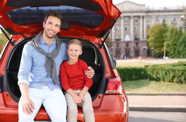 Молодий батько з милим хлопчиком сидить у багажнику автомобіля — стокове фото