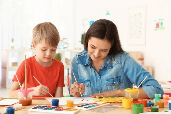 Schattige jongen met moeder schilderen aan tafel in de kamer — Stockfoto