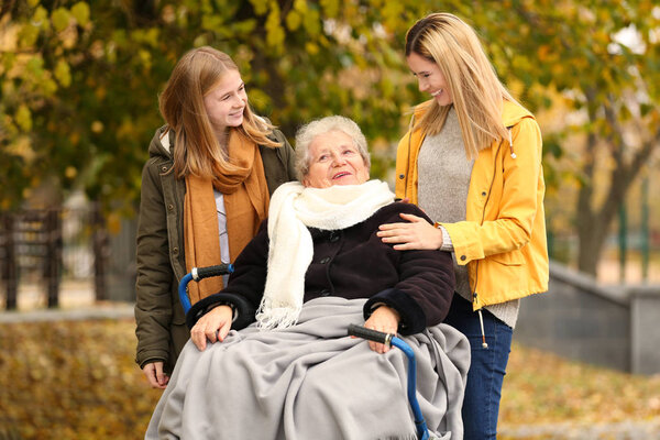 Elderly woman in wheelchair with her family outdoors on autumn day