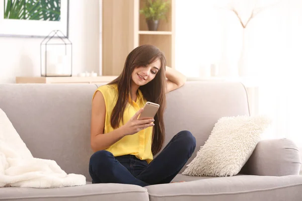 Mujer joven con teléfono en el sofá en casa —  Fotos de Stock