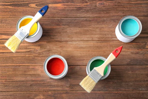 Multicolored paint in tin cans on wooden background, top view