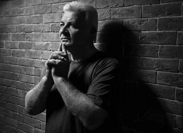 Красивий старший чоловік у повсякденному одязі на фоні цегляної стіни, чорно-білий ефект — стокове фото