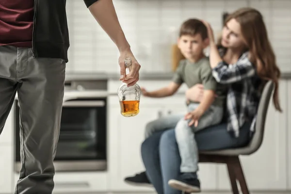 Чоловік тримає пляшку алкоголю, а дружина обіймає сина на фоні — стокове фото
