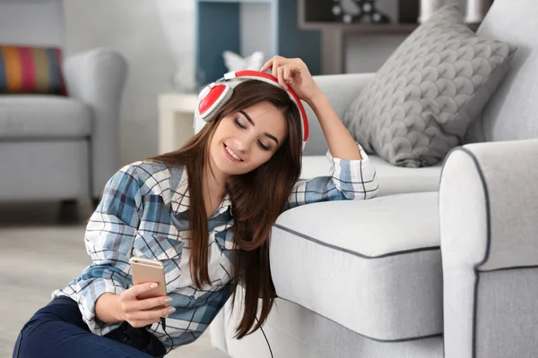 Молода жінка слухає музику через навушники біля дивана вдома — стокове фото