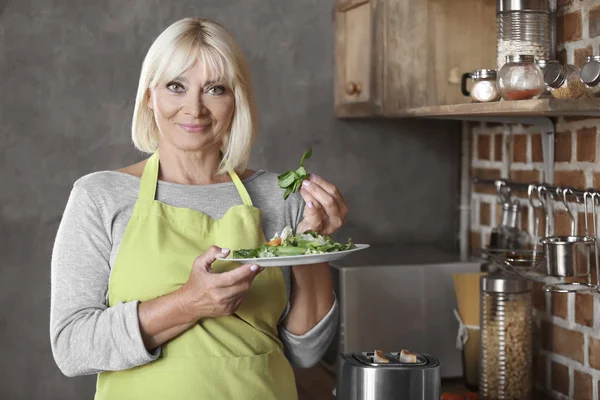 Attractive mature woman with plate of salad in kitchen — Stock Photo, Image