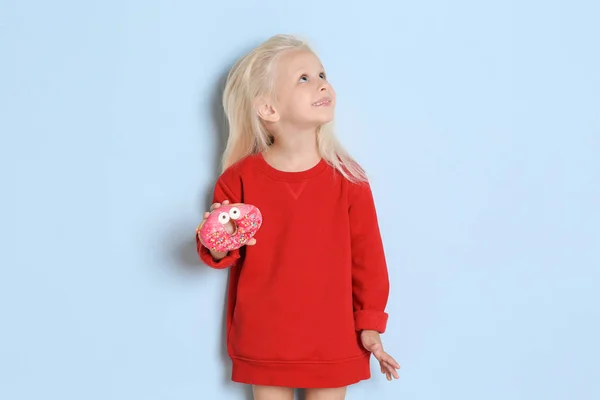 Маленькая девочка со сладким пончиком на цветном фоне — стоковое фото