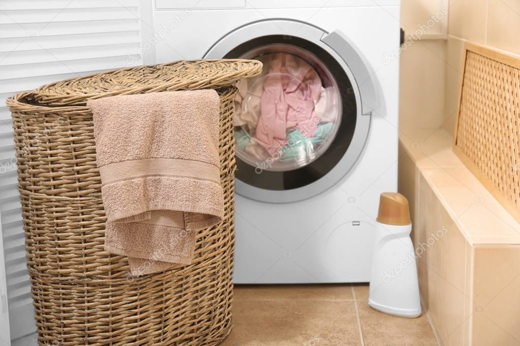Wicker basket with laundry near washing machine in bathroom