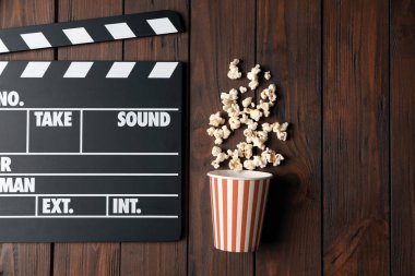 Clapperboard and popcorn on wooden background clipart