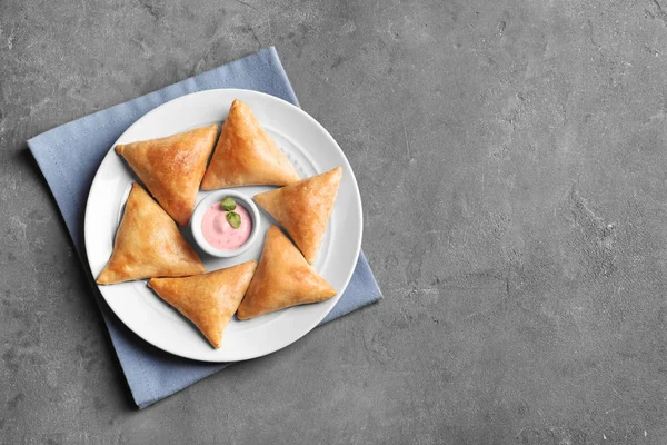 Placa con deliciosas samosas y salsa sobre fondo gris —  Fotos de Stock