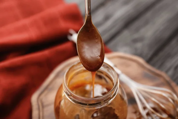 Cuchara con sabrosa salsa de caramelo sobre el frasco, primer plano —  Fotos de Stock