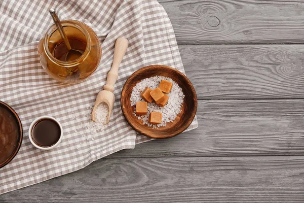 Piring dengan permen lezat dan botol karamel kosong di atas meja — Stok Foto