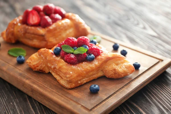 Board with tasty berry pastries on table