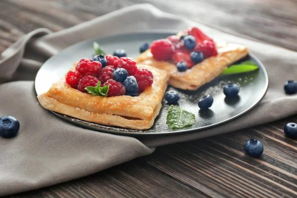 Plate with tasty berry pastries on table