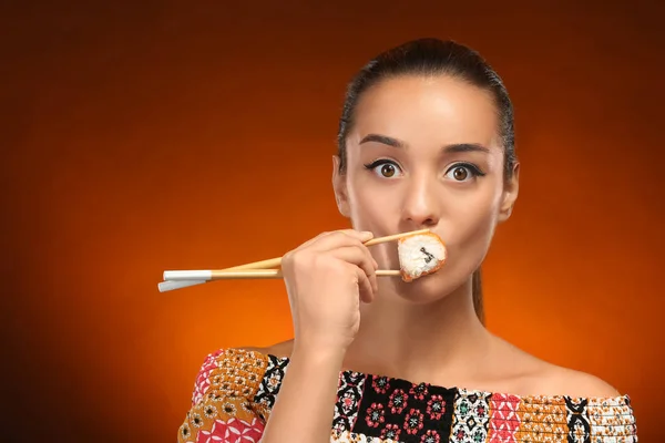 Mooie jonge vrouw met sushi roll op kleur achtergrond — Stockfoto