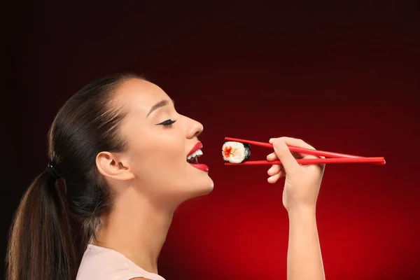 Beautiful young woman with sushi roll on color background — Stock Photo, Image