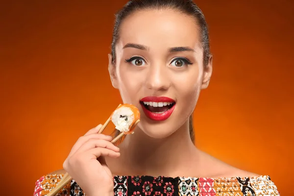 Krásná mladá žena s sushi roll na barvu pozadí — Stock fotografie
