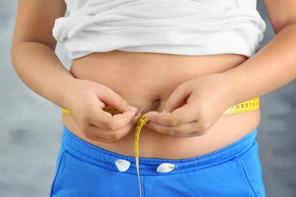 Overgewicht jongen meten taille op grijze achtergrond, close-up — Stockfoto