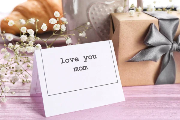 Cartão com palavras "Amo você mãe" e caixa de presente na mesa — Fotografia de Stock