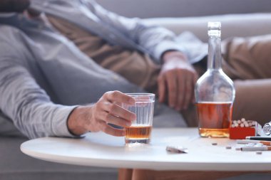 Elinde bardak viski ile kanepede yatan sarhoş adam. Alkolizm kavramı