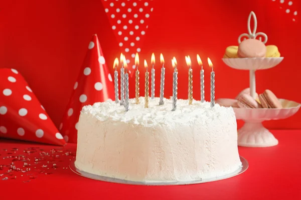 Födelsedagstårta med ljus på bordet mot röda väggen — Stockfoto