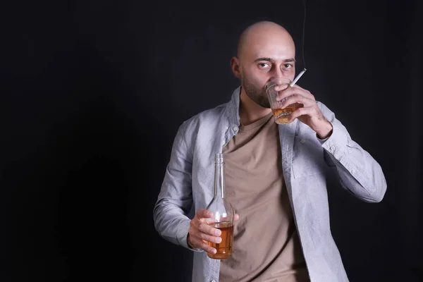 Man drinking whiskey and smoking cigarette on dark background. Alcoholism concept