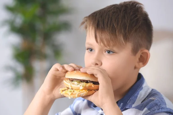 Overweight boy eating burger at home