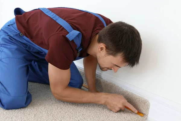 Worker using cutter while installing new carpet flooring in room — Stock Photo, Image