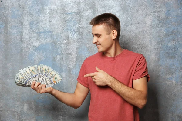 Joven sosteniendo dinero sobre fondo gris — Foto de Stock