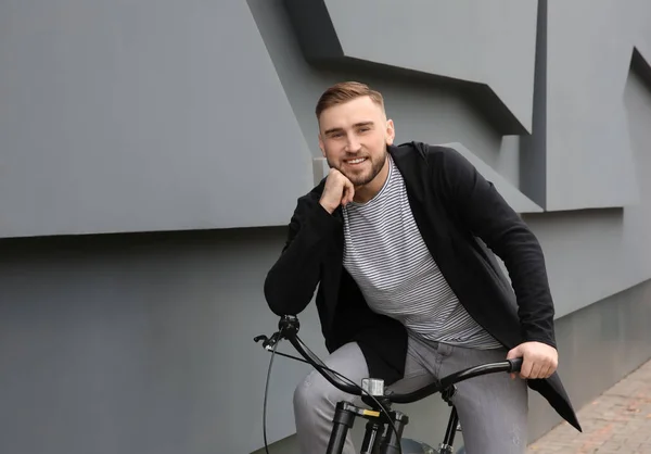 Bonito jovem hipster homem com bicicleta perto da parede ao ar livre — Fotografia de Stock