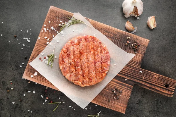 Wooden board with raw burger patty on table — Stock Photo, Image