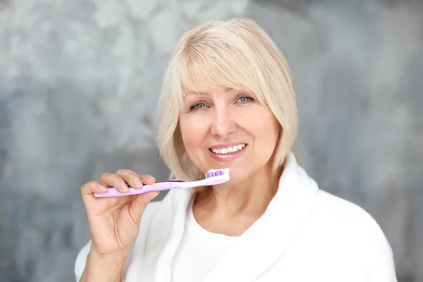 Зрелая женщина чистит зубы дома — стоковое фото
