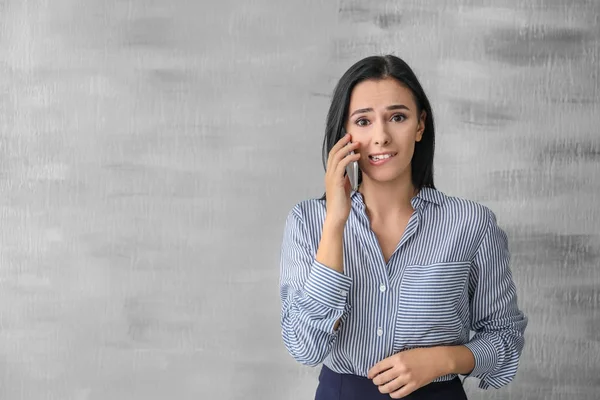 Emotionale junge Frau spricht per Handy auf grauem Hintergrund — Stockfoto