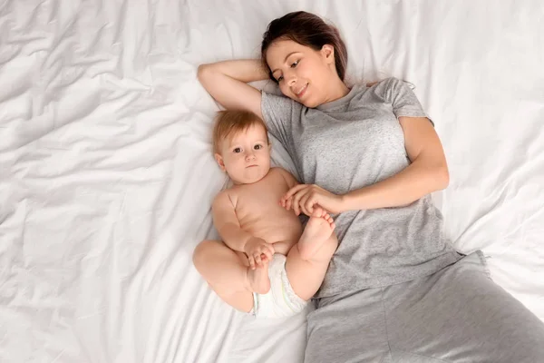 Jovem mãe e seu bebê bonito deitado na cama — Fotografia de Stock