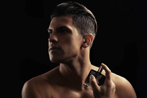 Schöner Mann mit einer Flasche Parfüm auf dunklem Hintergrund — Stockfoto