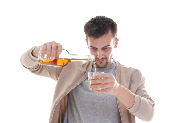 Un uomo che versa whisky in un bicchiere sullo sfondo bianco. Concetto di alcolismo — Foto Stock