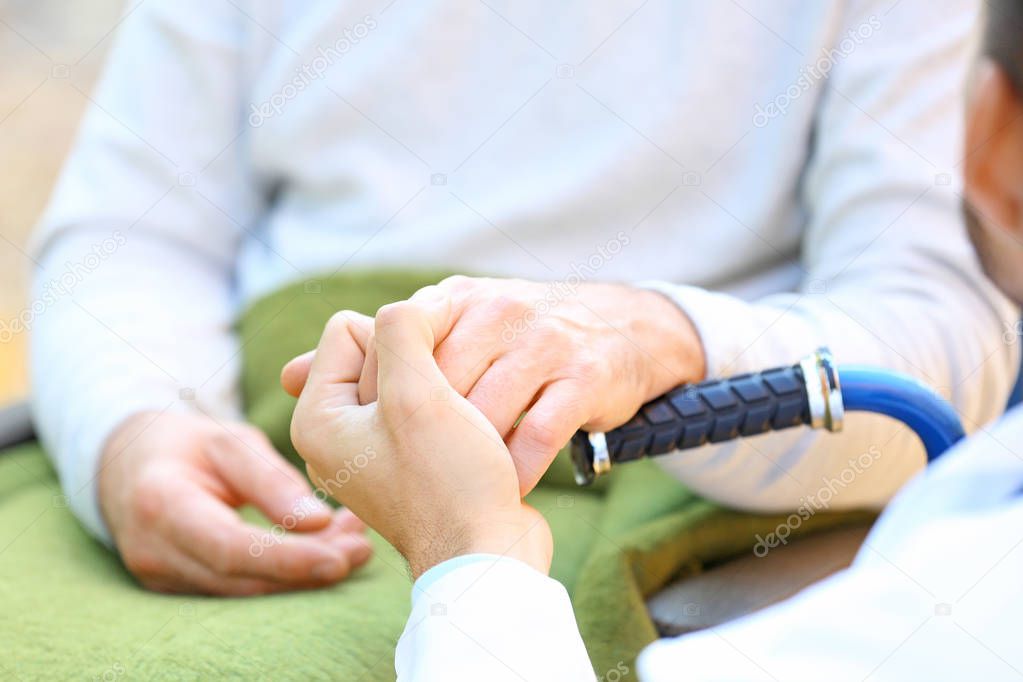 Young caregiver holding hands with senior man, closeup