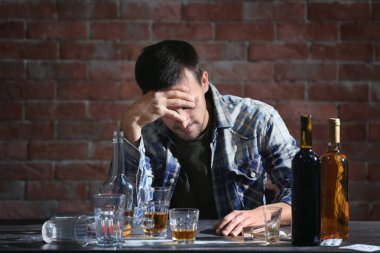 Alkol ve uyuşturucu ile masada oturan sarhoş adam. Alkolizm kavramı