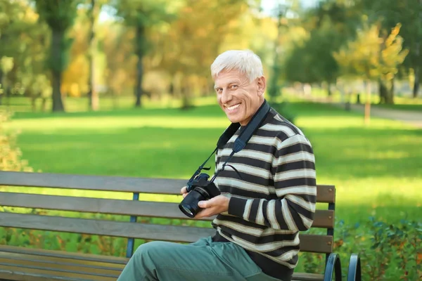 Стильный зрелый мужчина с камерой сидит на скамейке в осеннем парке — стоковое фото