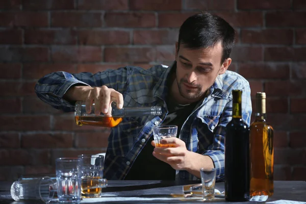 Man sitting at table and pouring whiskey into glass. Alcoholism concept